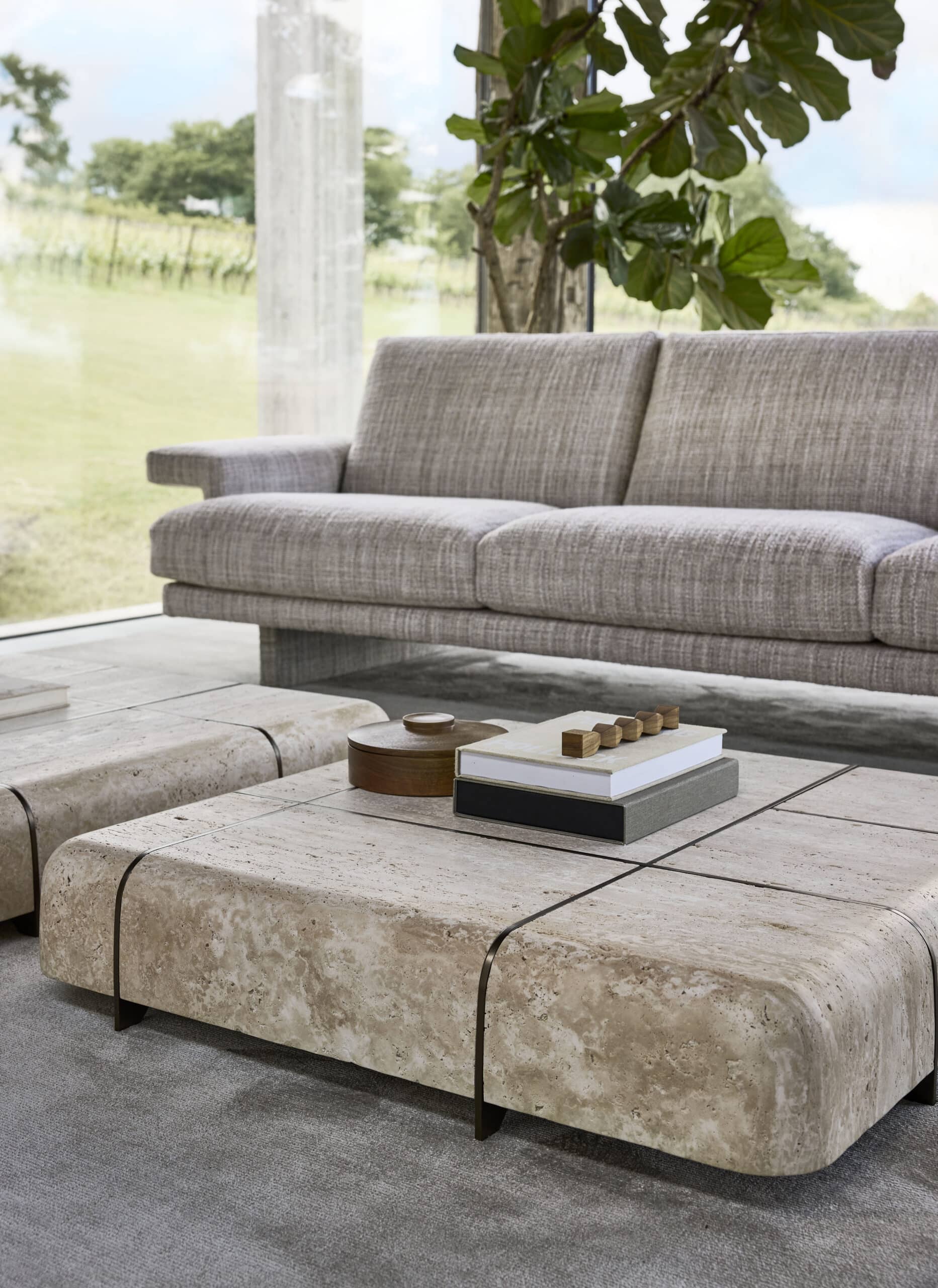 Linteloo fully opholstered Frank sofa and travertin stone Tessera coffee tables. The fabric of the sofa is textured. Shown in a living room with a lot of glass and robust wooden beams.