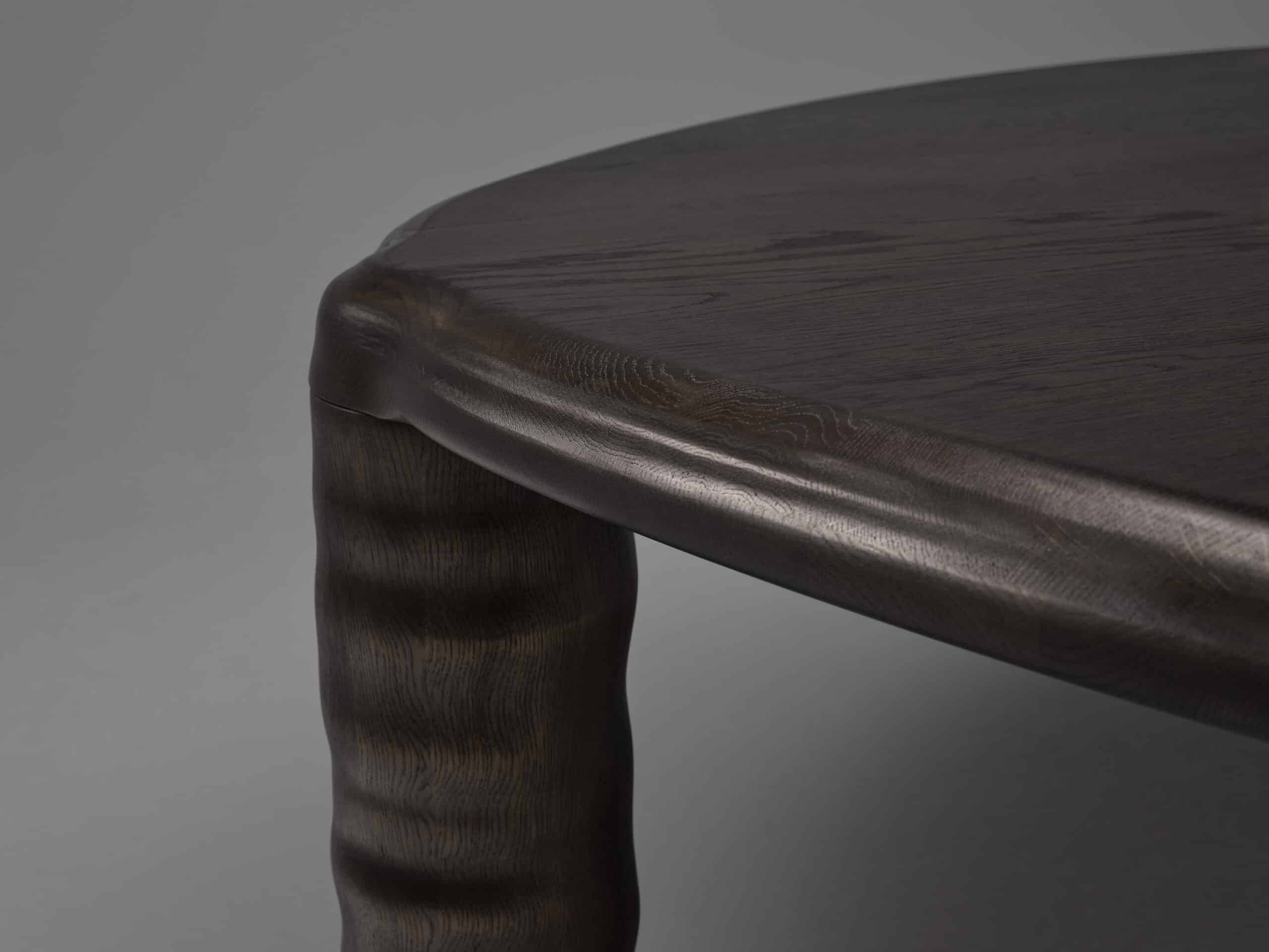 Detail image of the Linteloo Tembo table, made of solid oak wood in a dark brown finish. The table has three legs and a rounded triangle shape, with thick elephant trunk like legs.